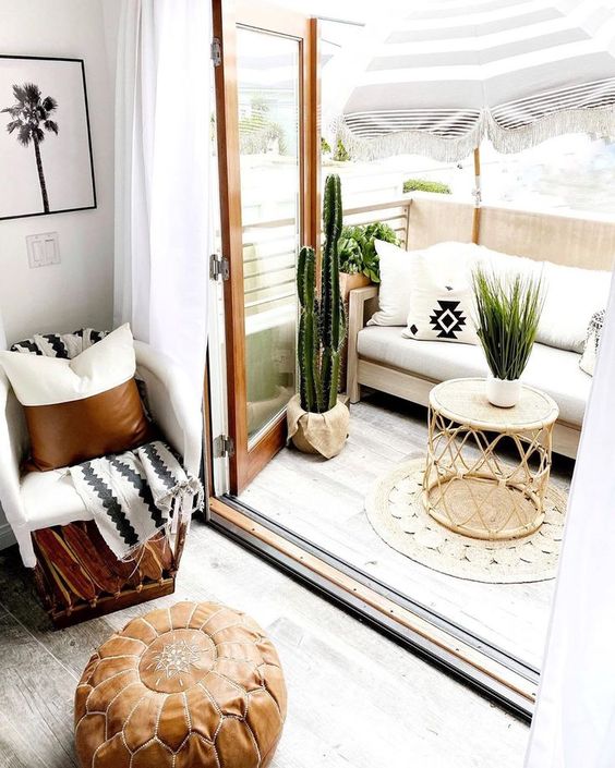 a neutral boho balcony with a white sofa, potted cacti and greenery, a rattan table, a jute rug and printed pillows