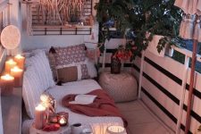 a neutral boho balcony with lights, candles, candle lanterns, a neutral sofa with lots of pillows, a crate with decor and greenery over the balcony