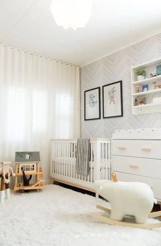 a neutral nursery with white and stained furniture, an open shelving unit, a wallpaper accent wall and some lovely and simple toys