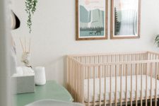 a pastel and neutral Scandinavian nursery with a gallery wall, a stained wood crib, a green dresser and potted greenery
