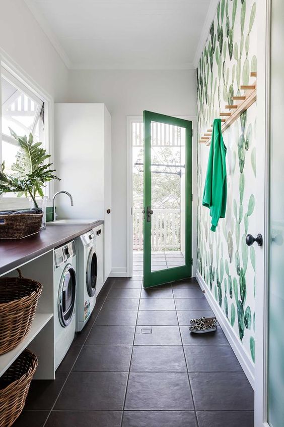 a pretty and bold laundry with an open storage unit that includes a washing machine and a dryer, a bold cactus accent wall and a large wardrobe