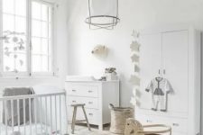 a pure white Scandinavian nursery with a dresser, a wardrobe, a crib, some stools and a pendant lamp plus pretty and cute decor