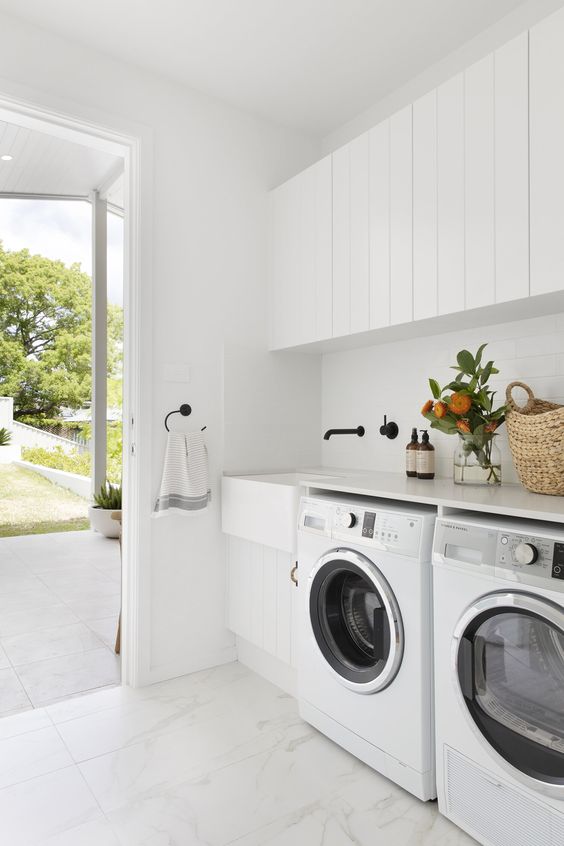 a pure white laundry room with shiplap cabinets, a sink with a black faucet and a washing machine and a dryer is a stylish space
