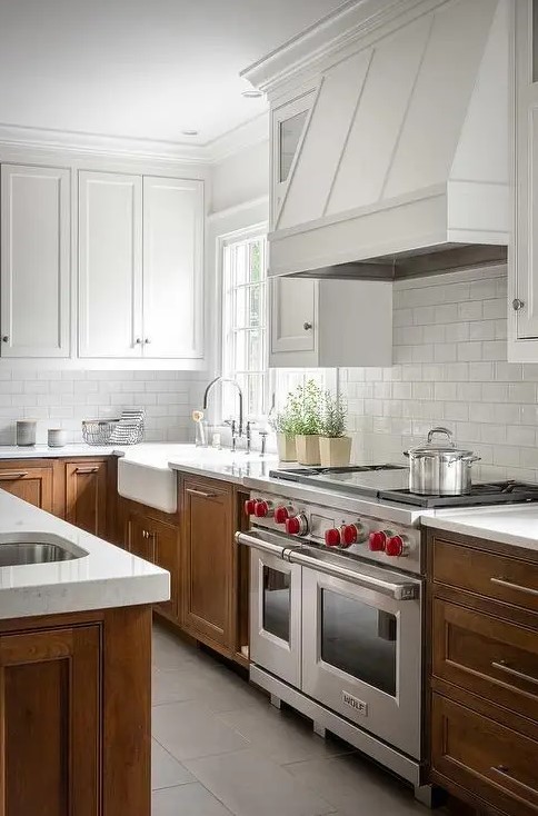 a rustic kitchen with upper white cabinets and lower stained ones, with white stone countertops and a white subway tile backsplash, a white hood