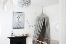 a small Nordic nursery with a black fireplace, a stained crib with a grey canopy, toys, grey and silver stars a basket with toys
