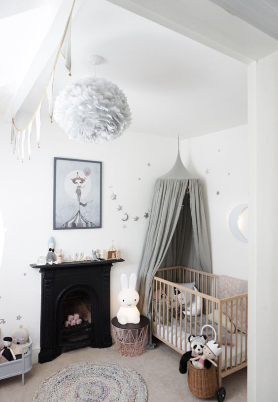 a small Nordic nursery with a black fireplace, a stained crib with a grey canopy, toys, grey and silver stars a basket with toys