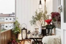a small Scandinavian balcony with a chair covered up with faux fur, candle lanterns, baskets and planted flowers