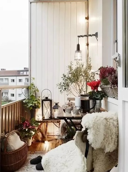 a small Scandinavian balcony with a chair covered up with faux fur, candle lanterns, baskets and planted flowers