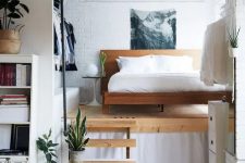 a small and chic modern loft bedroom with a wooden bed, an open closet and a cool artwork is a bold idea