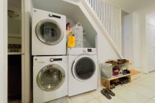 a small and cool laundry built under the staircase, with some storage shelves and a couple of machines