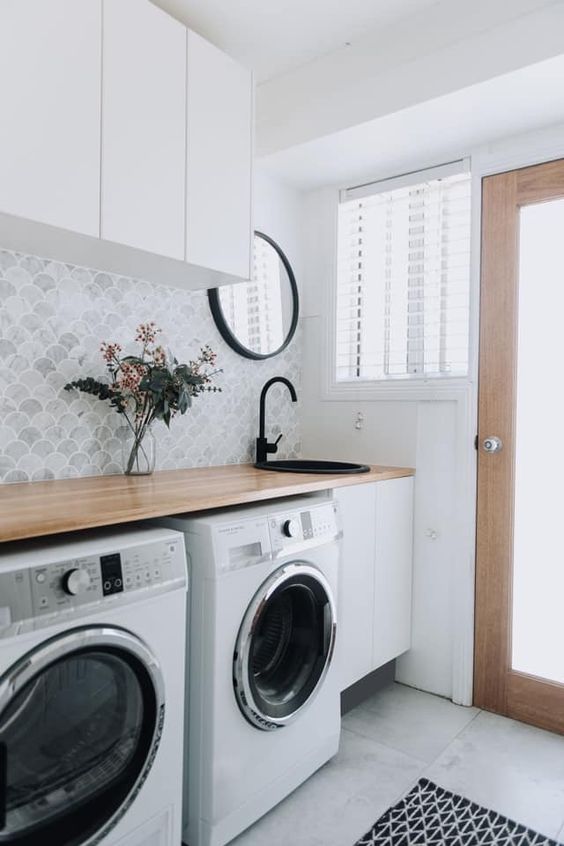 a small and functional laundry with sleek white cabinets, a washing machine and a dryer, a vanity with a black sink