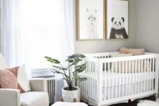 a small contemporary Scandi nursery with grey walls, white and creamy furniture, a printed rug, pink touches and a couple of prints on the wall