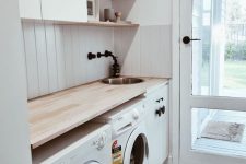 a small modern white laundry with sleek cabinets and round knobs, a wooden countertop, a glass door and white appliances
