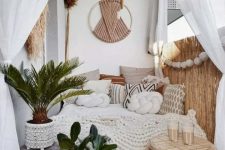 a small neutral boho balcony with a daybed with lots of pillows, some pampas grass and macrame, bamboo, potted plants and a lovely rattan stool