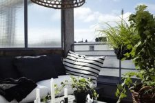 a stylish Nordic balcony with a black bench and black and white textiles, a wooden coffee table, a woven pendant lamp and some potted greenery