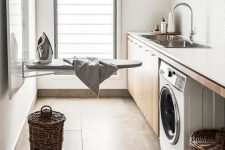 a stylish modern laundry with stained cabinets, a washing machine, an iron board that can be folded and a window
