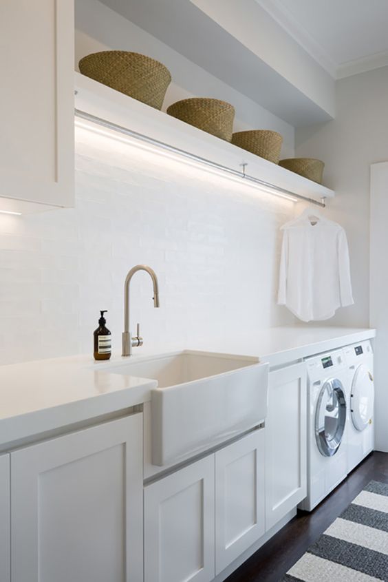 a stylish white laundry with shaker cabinets, open shelving with baskets, built-in lights and a striped rug