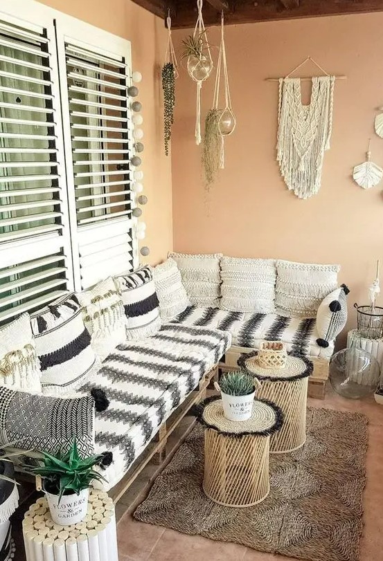 a terracotta-colored balcony with a corner pallet sofa with black and white upholstery anybody could sleep on, coffee tables and cork tables, macrame and hanging greenery