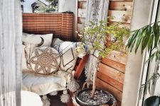 a tiny boho balcony with a bench with boho pillows and blankets, potted plants and greenery, a dream catcher, a jute rug and a wood slice table