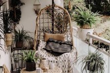a tiny boho balcony with rattan chairs and a table, lots of potted plants, pillows and blankets, lights and vases is a chic idea