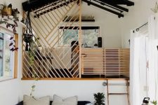 a tiny contrasting house with a living room and a bedroom up the stairs, with wooden screens to cover the space