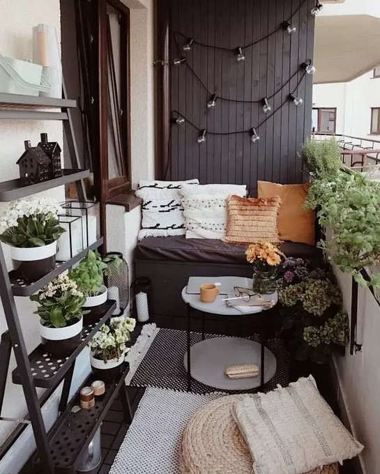 a tiny monochromatic balcony with black and white walls, black furniture, potted greenery and blooms and various pillows and rugs