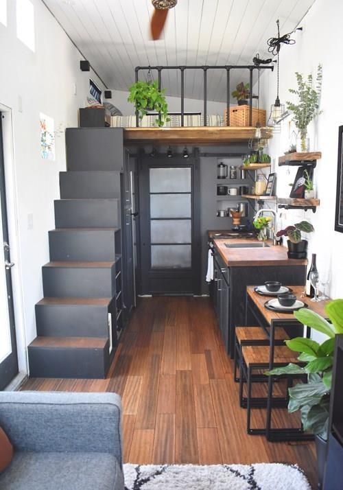 a tiny monochromatic home with a kitchen-living room below and a loft bedroom with a black staircase with storage is cool