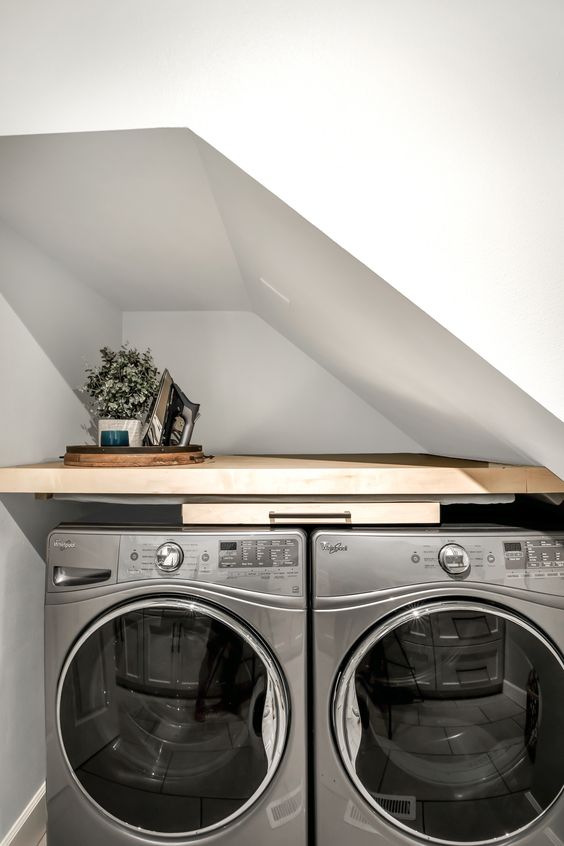 a tiny yet cool under the stairs laundry with a built-in shelf and a washing machine and dryer, with greenery and an iron