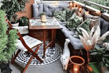 a tropical boho balcony with a corner sofa with grey upholstery and leaf print pilows, candle lanterns and lights, a printed rug