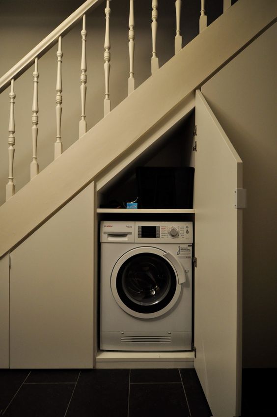 a vintage greige staircase with doors that hide a washing machine and some storage space - a small laundry