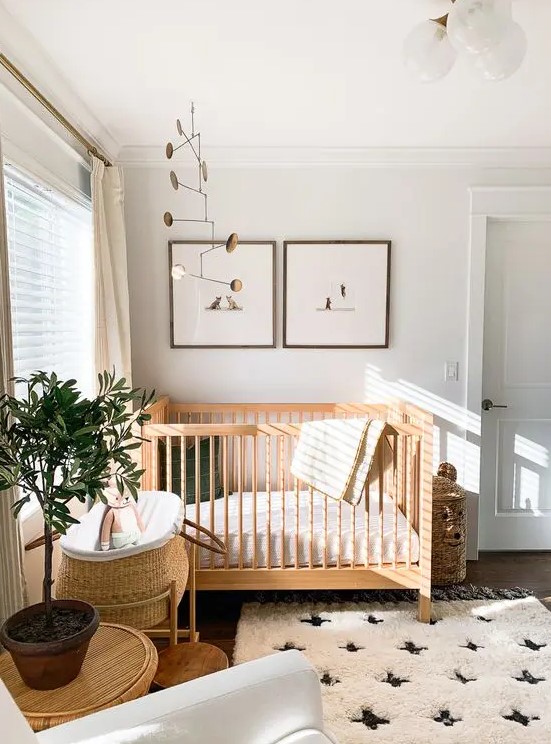 a welcoming Scandi nursery with stained furniture, a printed rug, a couple of artworks and a mobile, a basket for storage and a potted plant
