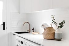 an edgy white laundry with sleek cabinets, black handles, a basket for storage, white appliances and built-in lights