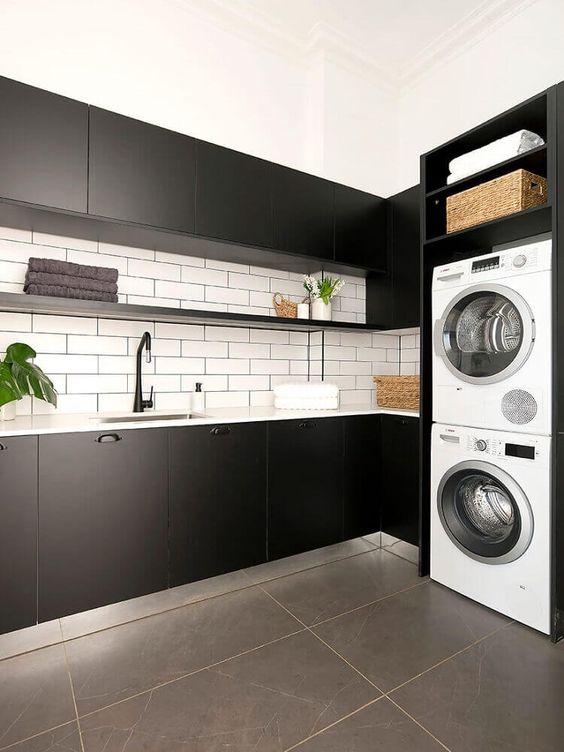 an elegant monochromatic laundry with matte blakc cabinets, white subway tiles on the backsplash, white appliances and baskets for storage