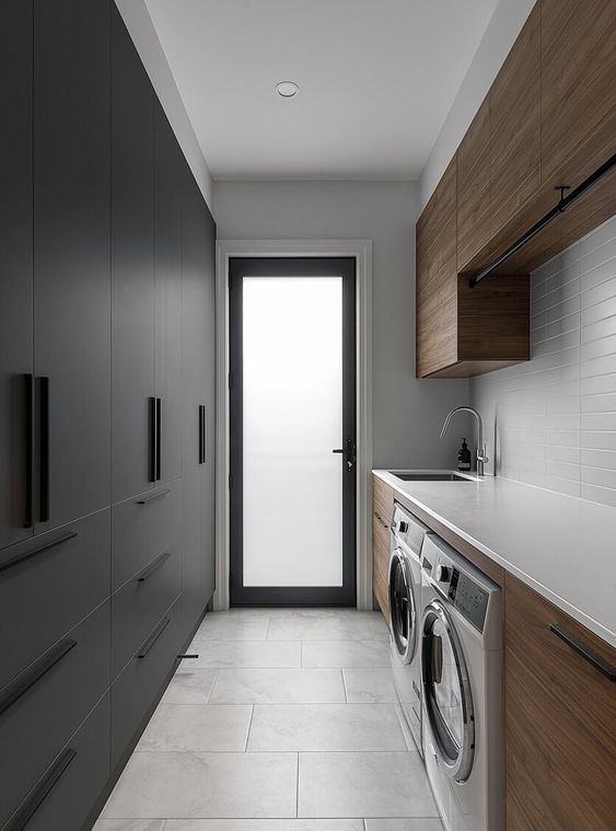 an ultimate minimalist laundry with sleek black wardrobes and drawers, stained cabinets, white countertops and a tile backsplash