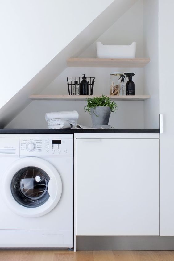 an under the staircase space with a washing machine and a dryer, with built-in shelves and no doors for a simple and practical laundry