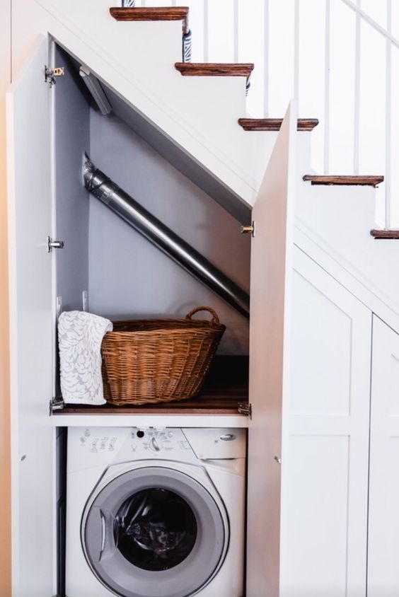 an under the stairs built-in laundry space with a built-in shelf for storage and a washing machine plus doors to hide it