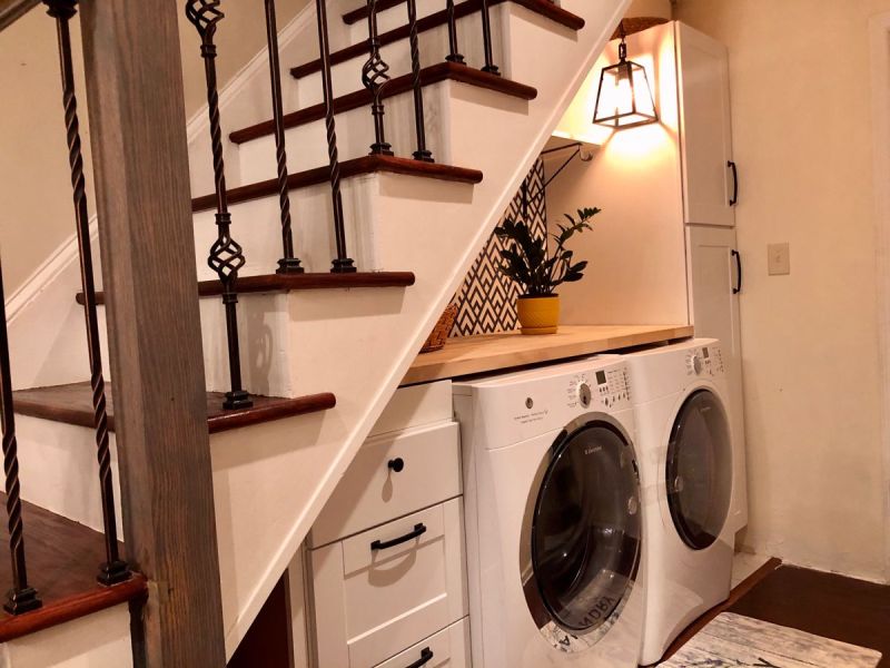 an under the stairs laundry with several storage cabinets, a built in countertop, a washing machine and a dryer