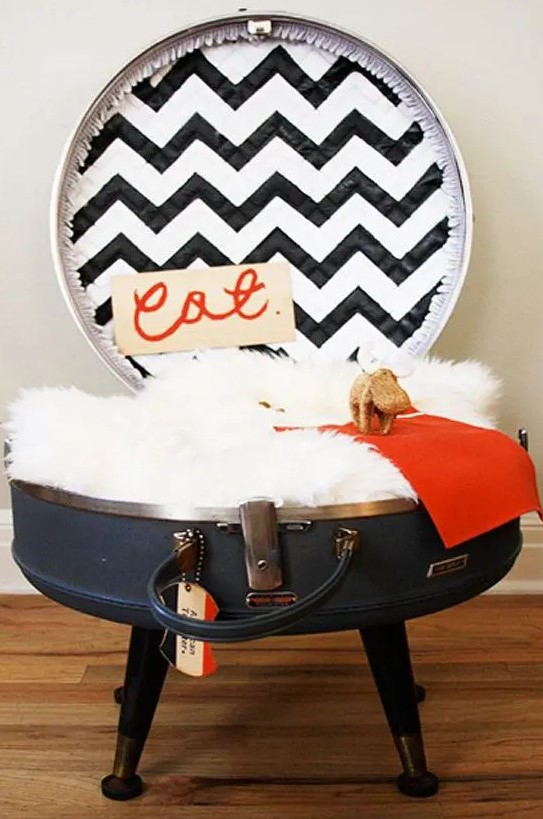 a cat bed made of a large round suitcase placed on legs, with a faux fur cushion, a blanket and a pretty chevron lid is a lovely idea