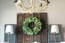 03 a rustic dining space with a dusty blue sideboard, vintage shutters, a greenery wreath and potted greenery, a jute wrapped chandelier