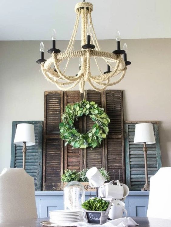 a rustic dining space with a dusty blue sideboard, vintage shutters, a greenery wreath and potted greenery, a jute wrapped chandelier