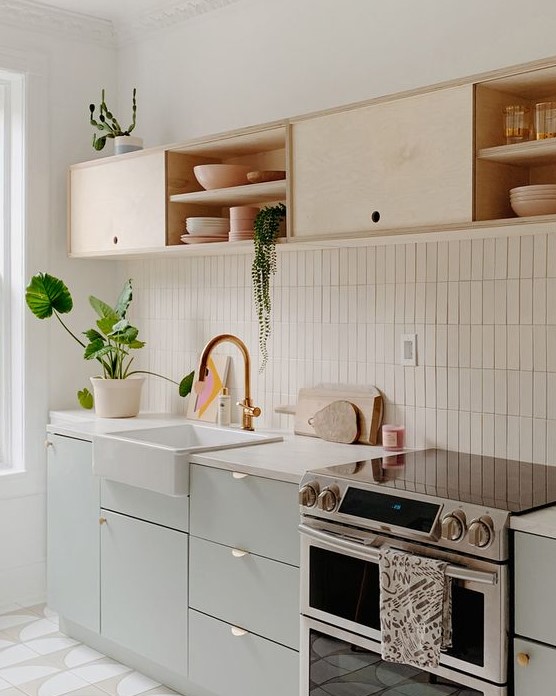 a chic kitchen in dove grey and light colored plywood, with white countertops and a white skinny tile backsplash