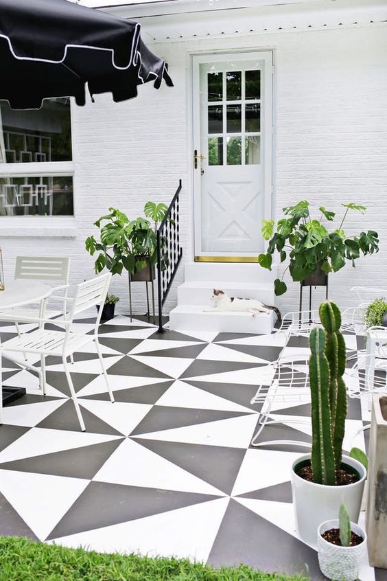 a black and white terrace with a geo tile floor, white garden furniture, a black umbrella, potted greenery and cacti