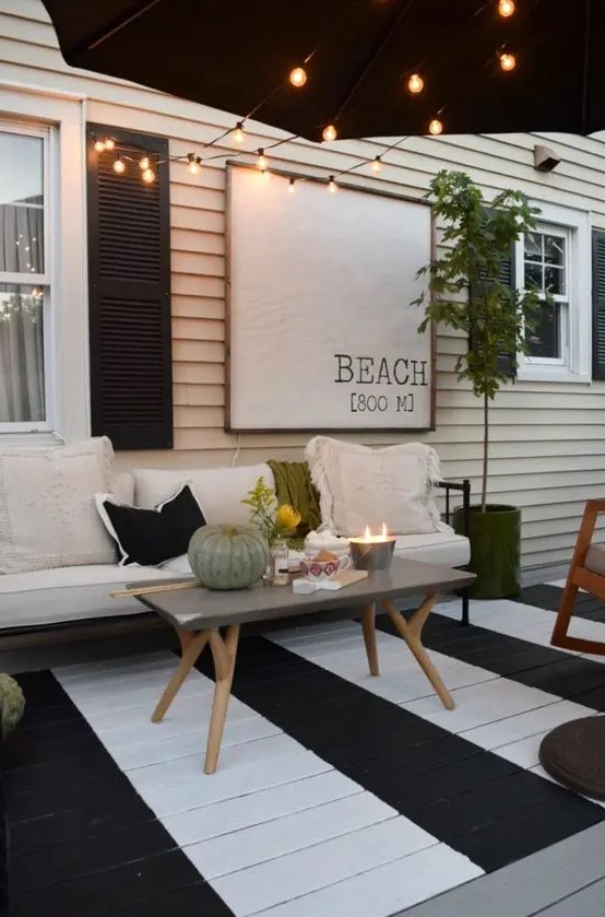 a black and white terrace with a painted deck, a black and white bench, a concrete table and lights over the space