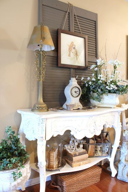 beautiful vintage cottage decor with taupe shutters, a refined carved console table, vintage books, candles and table lamps
