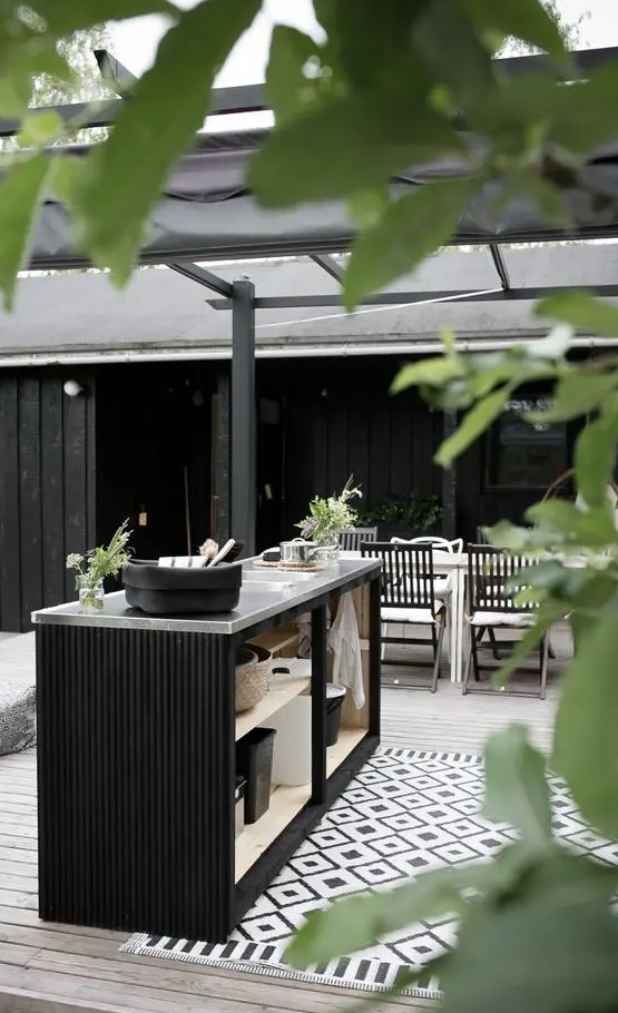 a chic Nordic outdoor space with a deck, a whitewashed dining table and black chairs, a black kitchen island