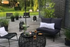 09 a contrasting terrace with a grey wooden deck, black metal furniture, white pillows, an umbrella and a black wicker table