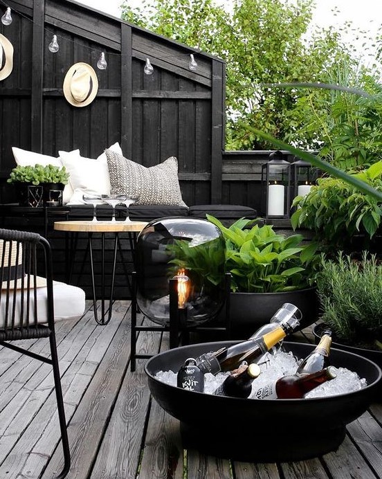 a dark Nordic terrace with black walls, planters and bowls, metal and wooden furniture, a catchy floor lamp and greenery that refreshes the space