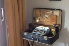 10 a mini desk made of a vintage suitcase, with a typewriter inside, some lights, cacti and a vintage camera and potos for decor