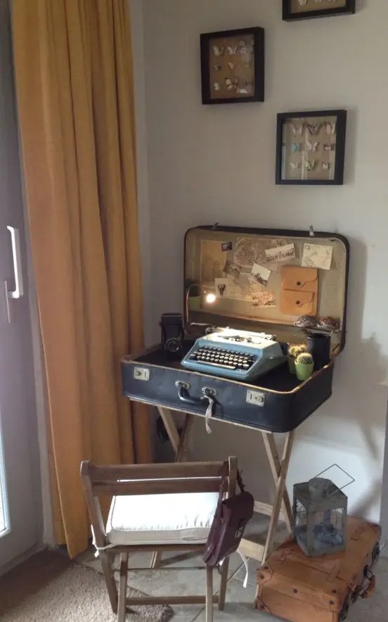 a mini desk made of a vintage suitcase, with a typewriter inside, some lights, cacti and a vintage camera and potos for decor