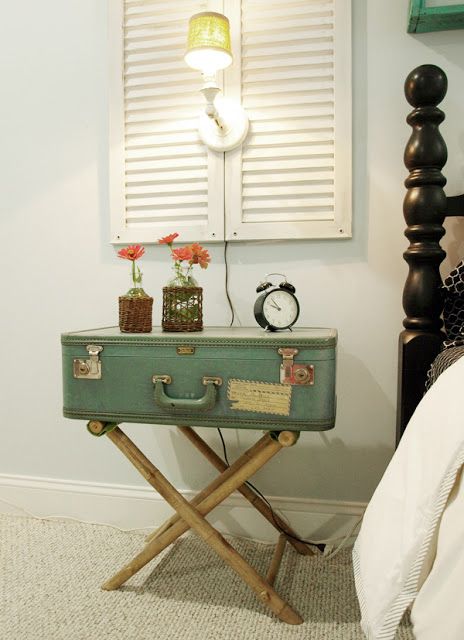 a nightstand of a green suitcase and trestle legs, with vases and a clock is a pretty vintage touch to your bedroom